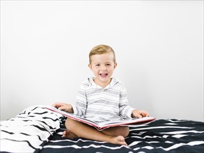 Boy (4-5) sitting on bed and holding book