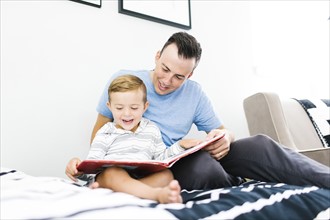 Father and son (4-5) sitting on bed and reading book
