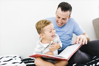 Father and son (4-5) sitting on bed and holding book