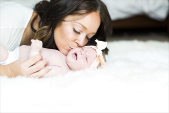 Mother kissing daughter (0-1 months) on bed