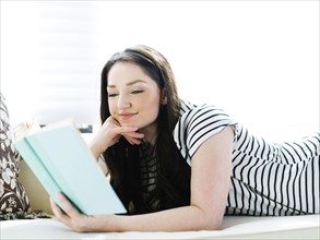 Woman lying on couch and reading book
