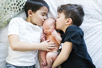 Two boys (6-7, 8-9) kissing baby brother (2-5 months)