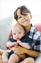 Young boy (6-7) holding brother (2-5 months)