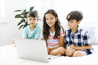 Siblings (10-11, 6-7, 8-9) sitting in bed and using computer