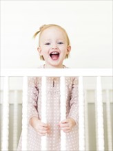 Content small girl ( 12-17 months)  with mouth open standing in crib
