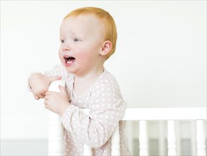 Small girl ( 12-17 months) with red hair standing in crib