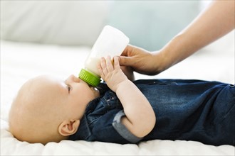Side view of baby boy ( 12-17 months) being fed by woman with bottle of milk