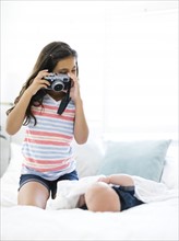 Girl (10-11)  taking photo of her small brother (12-17 months)  lying on bed