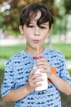 Boy (6-7) drinking milk with straw in park