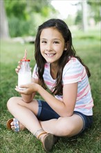Girl (10-11) sitting on grass holding glass of milk