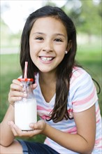 Girl (10-11) in park holding glass of milk with straw