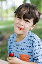 Boy (6-7) eating strawberry in park