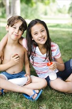 Boy (6-7) and girl (10-11) sitting on grass in summer