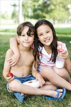 Boy (6-7) and girl (10-11) sitting arm around on grass in summer