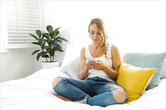 Young woman with mobile phone sitting on bed
