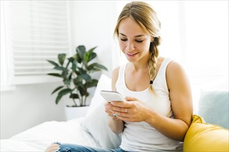 Young woman with mobile phone sitting on bed