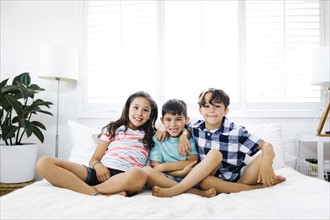 Portrait of smiling brothers ( 6-7, 8-9 ) and sister ( 10-11 ) sitting on bed