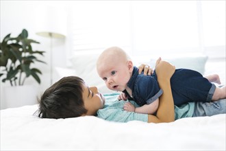 Boy ( 8-9 ) lying on bed and embracing brother ( 2-5 months )