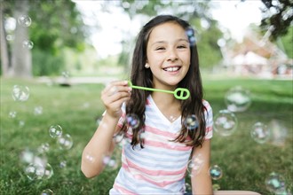 Portrait of girl ( 10-11 ) sitting in meadow and blowing soap bubbles