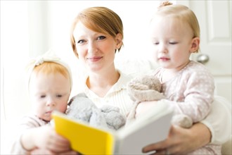 Portrait of mother reading book to daughters ( 12-17 months )