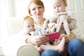 Portrait of mother using smart phone with daughters ( 12-17 months )