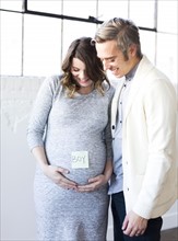 Portrait of men and smiling pregnant woman with adhesive note on belly