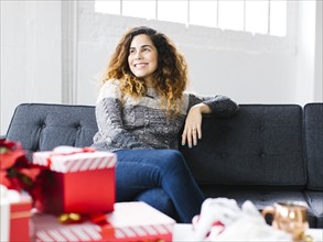 Happy woman on sofa with Christmas gifts in foreground