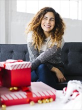 Happy woman on sofa with Christmas gifts in foreground