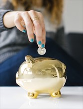Woman dropping coin into gold piggy bank