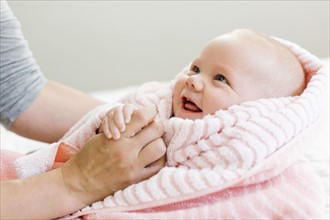 Baby boy (12-17 months) in pink blanket holding mom's hand and smiling