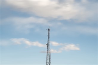 Top of communications tower with sky and clouds in background