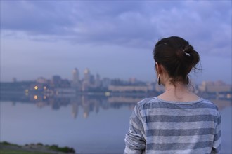 Ukraine, Dnepropetrovsk, Rear view of woman looking at city skyline at dusk