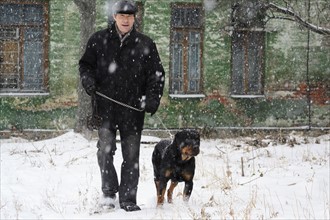 Ukraine, Dnepropetrovsk, Man walking in snow with rottweiler