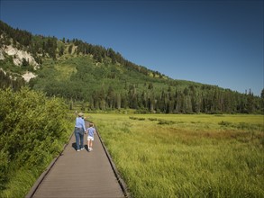 USA, Utah, Lake City, Girl (4-5) with grandmother walking on boardwalk through wetland