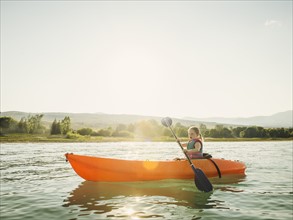 Girl (4-5) kayaking on lake at sunset