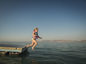 Girl (4-5) jumping into lake from pier