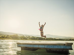 Girl (4-5) jumping into lake from pier