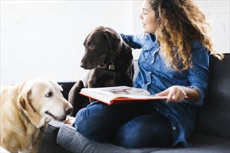 Woman sitting with dogs in living room and reading book