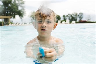 Boy (6-7) playing with squirt gun in swimming pool