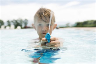 Boy (6-7) playing with squirt gun in swimming pool