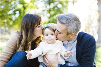 Portrait of parents kissing daughter (12-17 months) in park