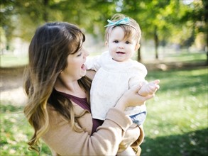 Portrait of mother carrying daughter (12-17 months) in park