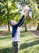 Father throwing daughter (12-17 months) up in air in park