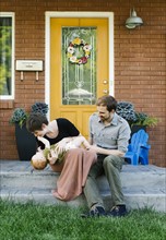 Parents with daughter (12-17 months) sitting in front of house