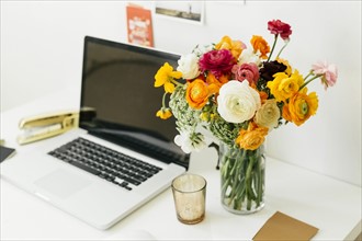 Flowers in jar near laptop in office