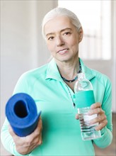 Portrait of senior woman holding mat and bottle with water
