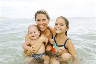 Mother and children (6-7, 12-17 months) embracing in sea