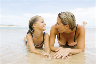 Mother lying with daughter (6-7) on beach