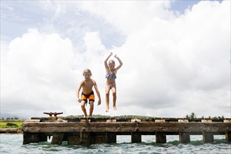 Boy (8-9) and girl (6-7) jumping into sea from jetty