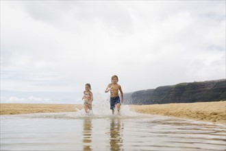 Boy (8-9) and girl (6-7) running through sea